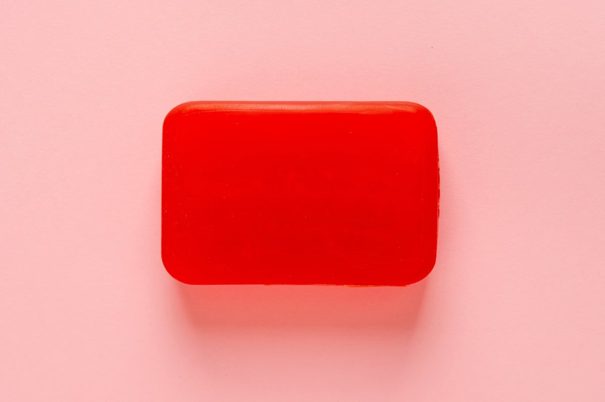Red Soap Bar, Body Care Cosmetic, Fruit Flavored Soapy Detergent, Solid Shampoo, Red Translucent Glycerin Soap on Pink Background